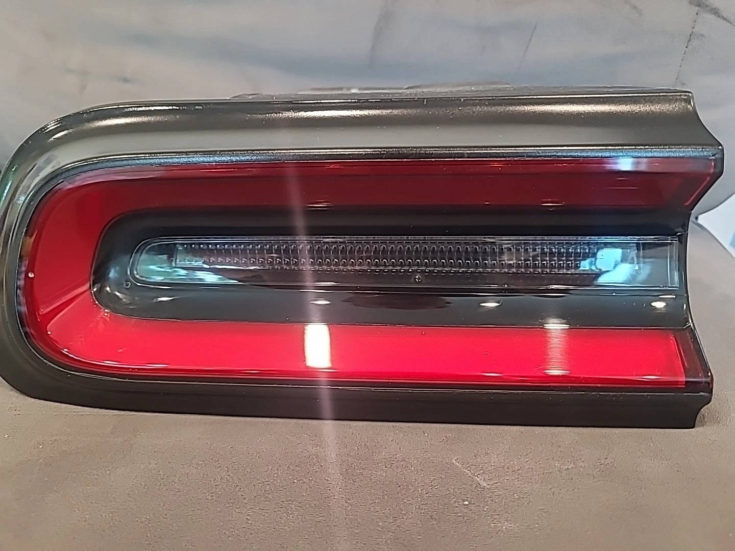 Close-up of a red car's rear tail light with a clear lens and horizontal light strips.