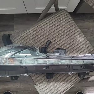 A clear car headlight assembly resting on a striped fabric surface.