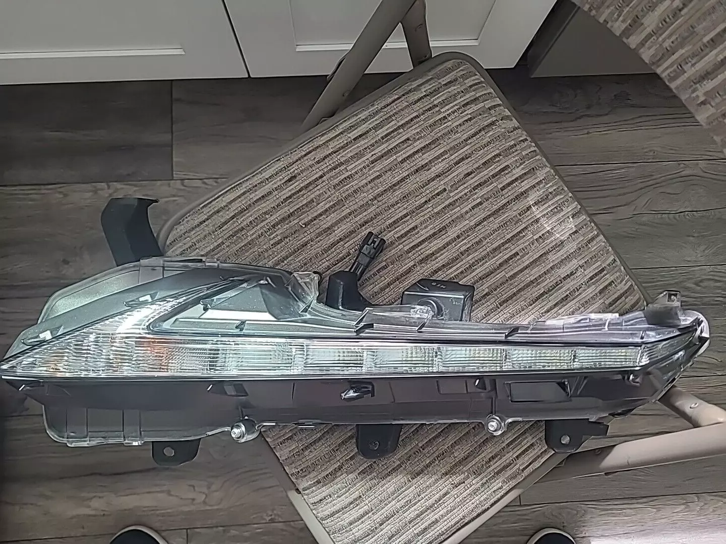 A clear car headlight assembly resting on a striped fabric surface.