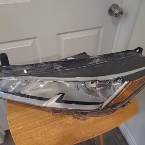 A modern car headlight assembly placed on a wooden surface indoors.