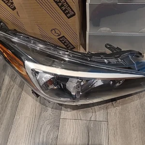 A detached car headlight resting on a wooden floor.