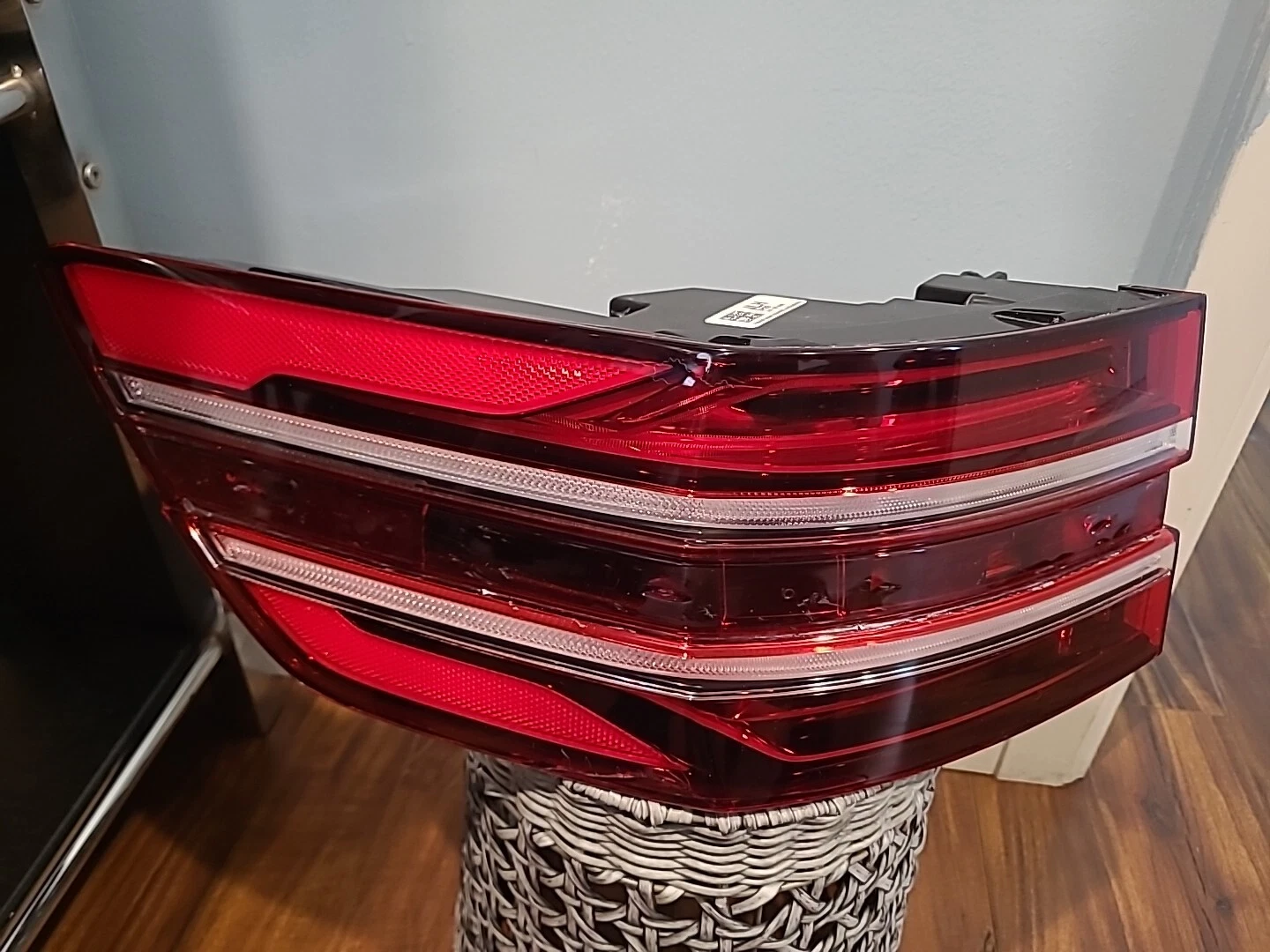 Close-up of a modern car's red taillight with clear sections, placed indoors on a wicker stand.