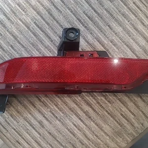 Close-up of a red car reflector with mounting brackets on a textured surface.
