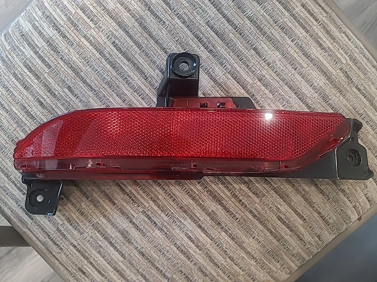 Close-up of a red car reflector with mounting brackets on a textured surface.