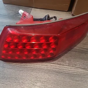 Close-up of a red car tail light with wiring on a wooden floor.