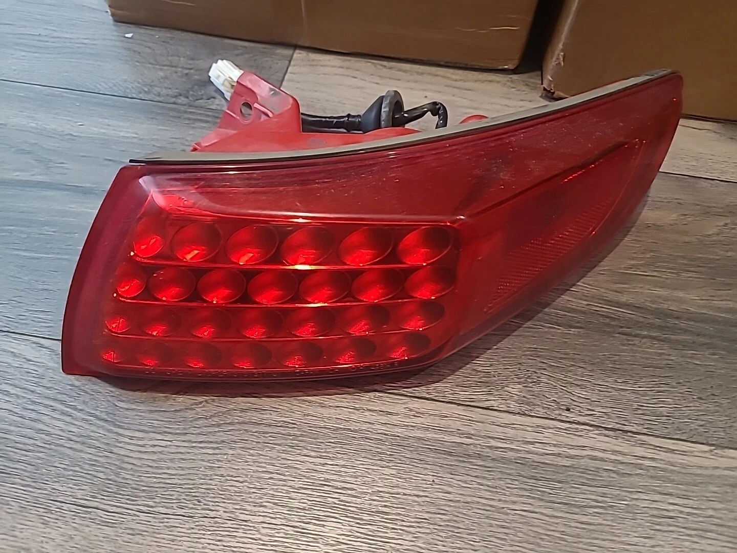 Close-up of a red car tail light with wiring on a wooden floor.