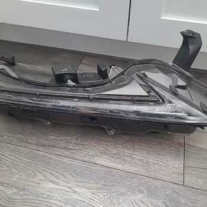 A damaged black car headlight assembly on a wooden floor.